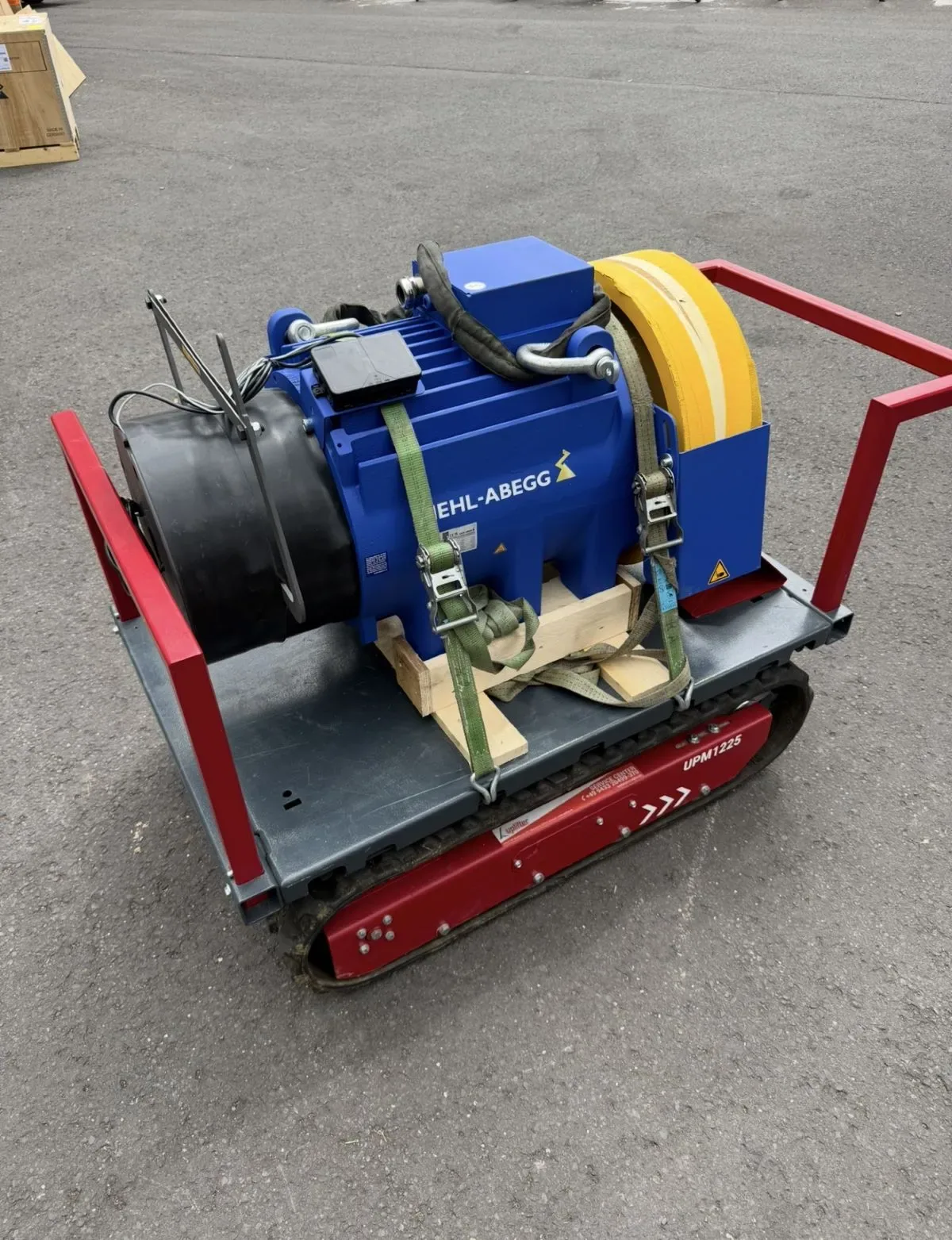 Blauer Ziehl-Abegg Aufzugsantrieb verzurrt auf einem roten Raupentransporter an der Baustelle