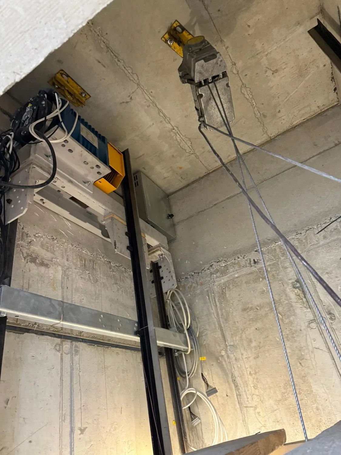 Blick in einen Aufzugsschacht im Rohbau mit Führungsschienen, Verkabelung und Tragseilen